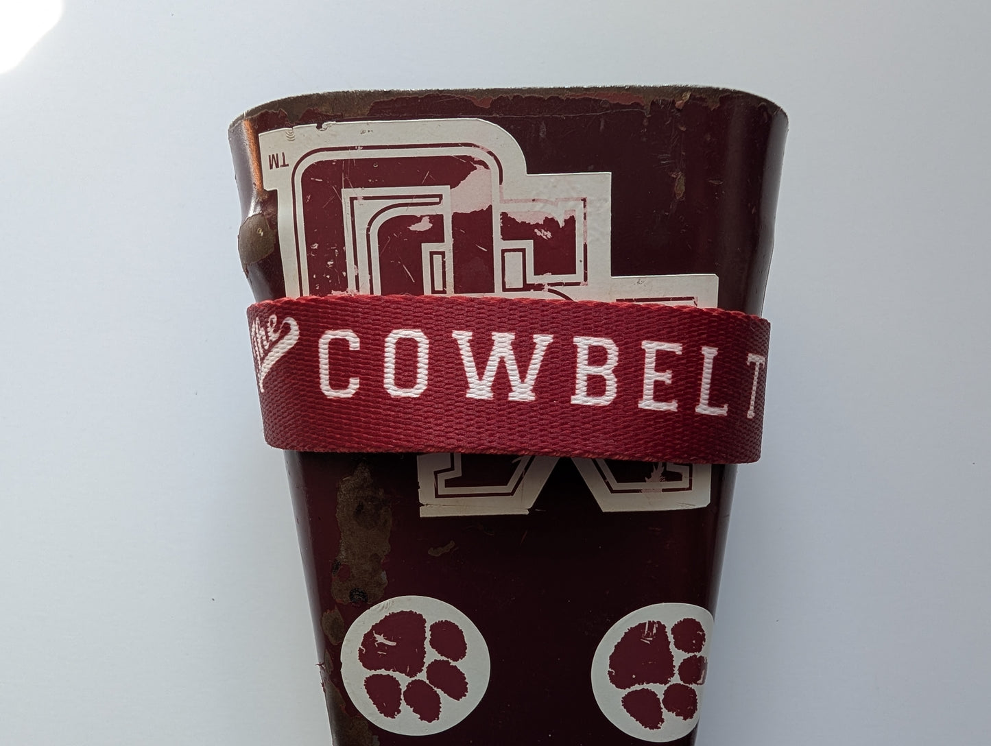Cowbell with a maroon strap labeled 'Cowbell' on a white background