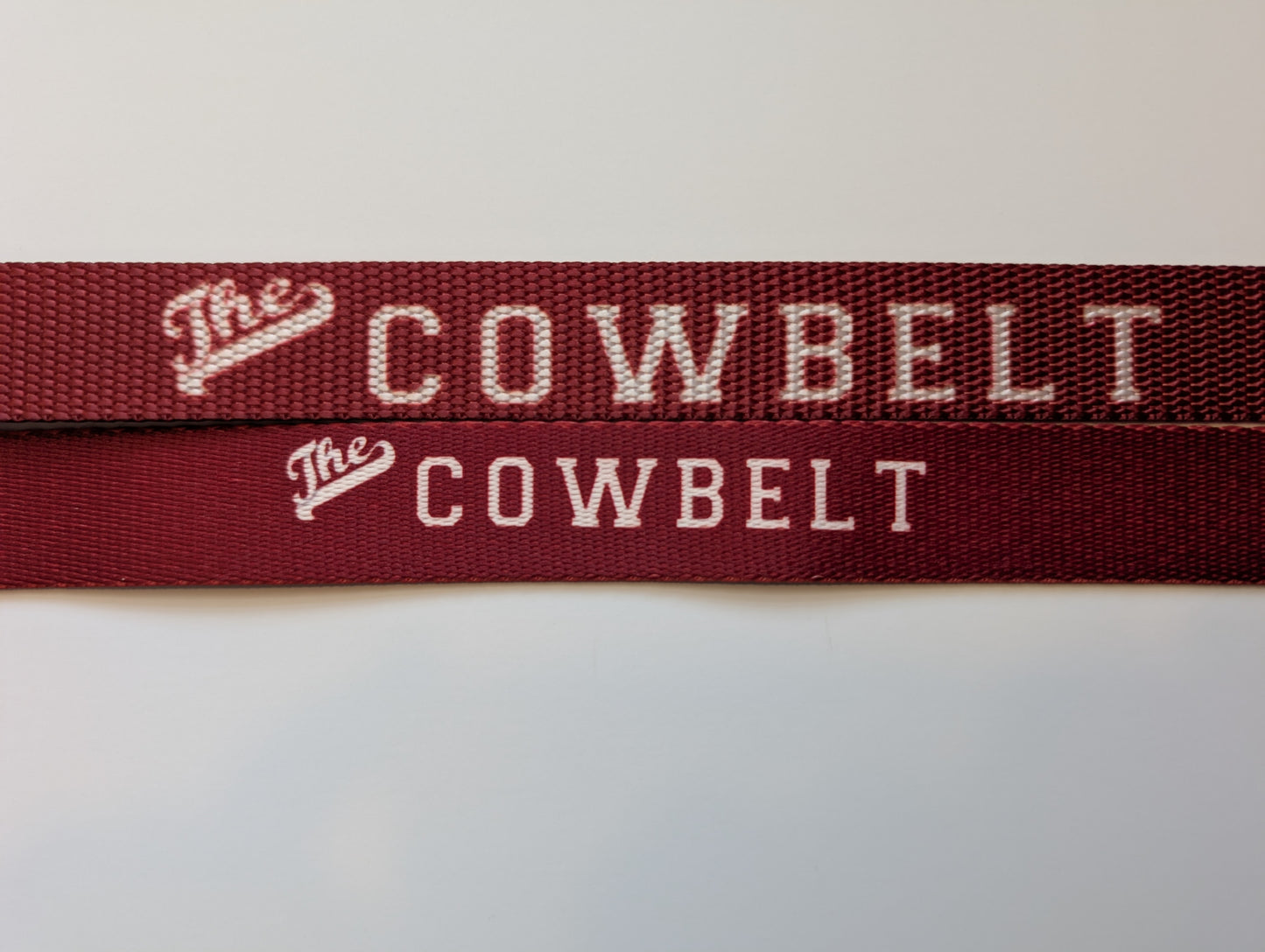 Close-up of maroon straps with 'The Cowbelt' branding on a white background comparing old and new versions
